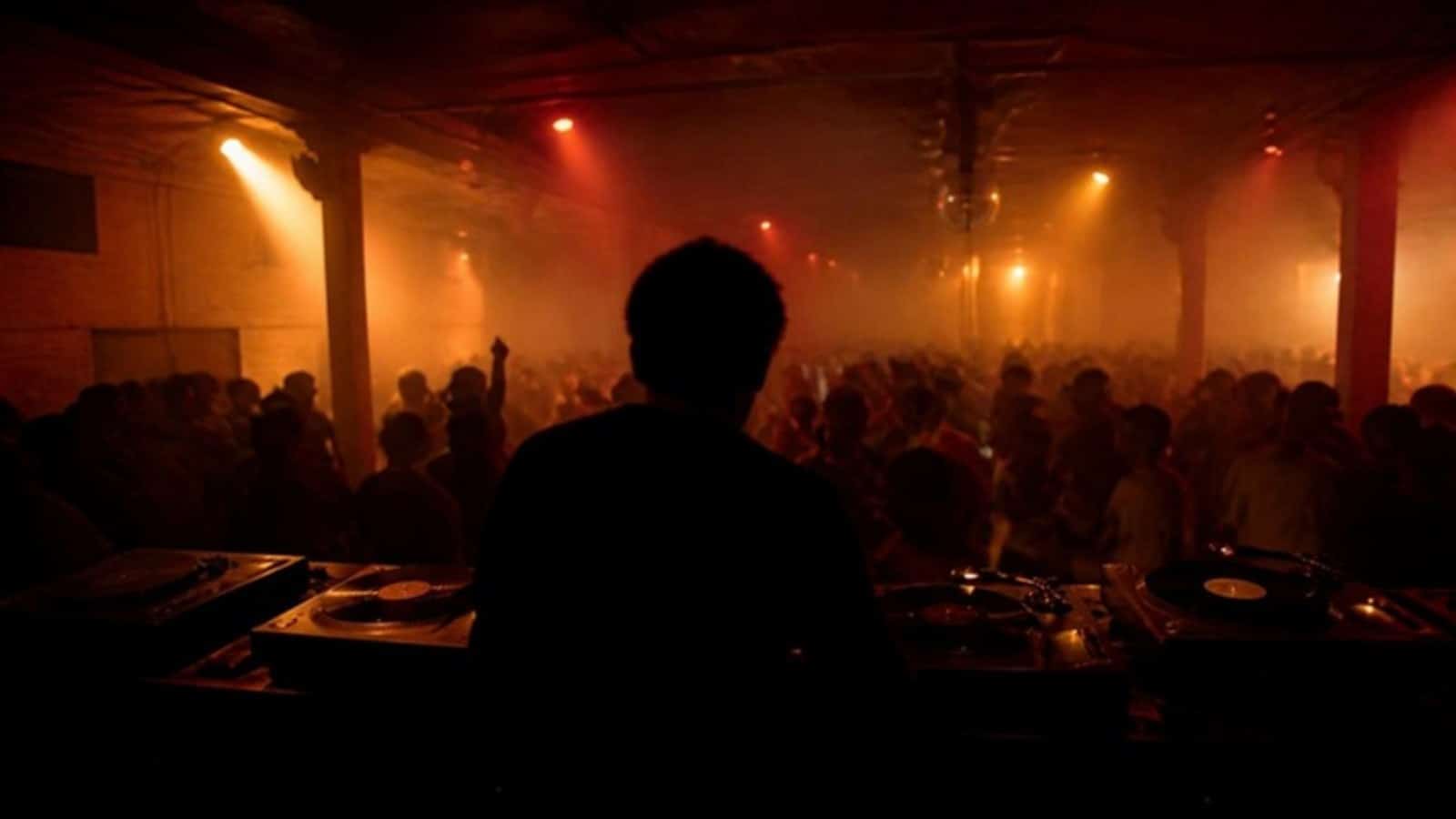 A dimly lit underground warehouse nightclub evoking early Chicago house music, with a DJ silhouette behind the decks under amber stage lights and a crowd dancing in the haze